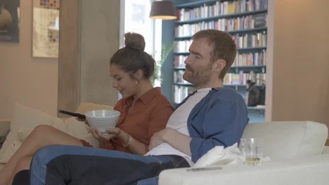 Handheld shot of couple changing channels with remote control while watching TV Stock Footage 114842381
