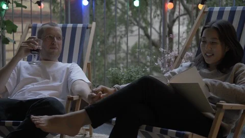 Handheld shot of couple drinking wine and reading book while sitting on chair Vídeo Stock 114842937