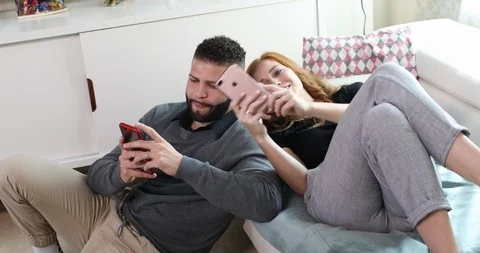 Handheld shot of couple having fun while using mobile phone in living room Stock Footage 119742387