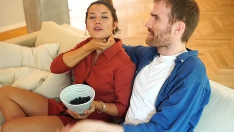 Handheld shot of couple talking and eating while sitting on the sofa 스톡 동영상 114884532