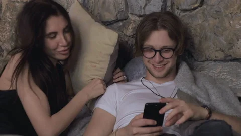 Handheld shot of couple talking and using phone while lying on bed at home Stock Footage 137732087