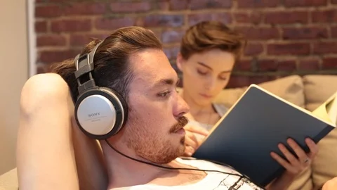 Handheld shot of couple using laptop and reading book while sitting on couch Stock Footage 114862095