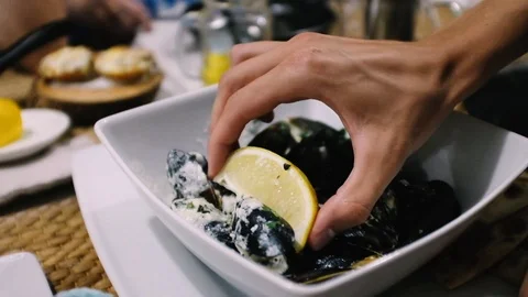 Handheld shot of cropped hand squeezing lemon over mussels in bowl on table Stock Footage 122519588