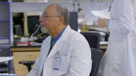 Handheld shot doctors discussing reports over desktop computer at hospital Stock Footage