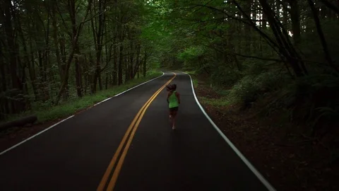Handheld shot of female athlete running on road in forest Stock Footage