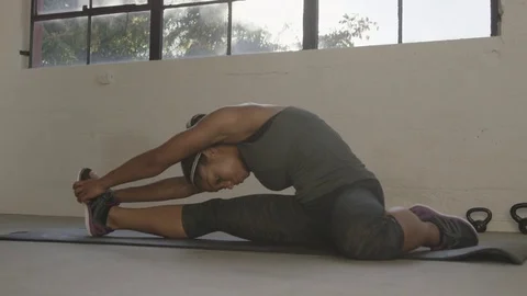 Handheld shot of female athlete stretching body while sitting on exercise mat at Stock Footage