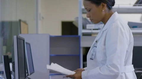 Handheld shot of female doctor holding reports while standing at desk in Stock Footage