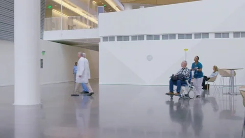 Handheld shot of female doctor pushing patient sitting on wheelchair while Stock Footage