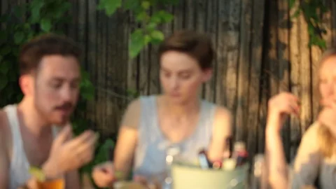 Handheld shot of friends talking and eating while sitting at table in backyard Stock Footage 114862292