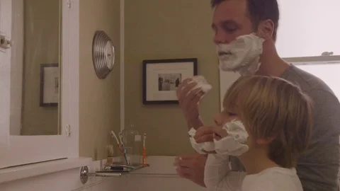Handheld shot of happy father assisting son in applying shaving cream on face at Stock Footage