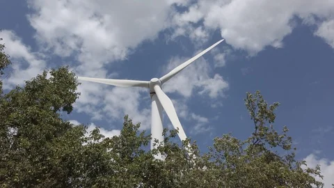 Handheld shot of huge spinning windmill surrounded by trees against sky Stock Footage 120045461
