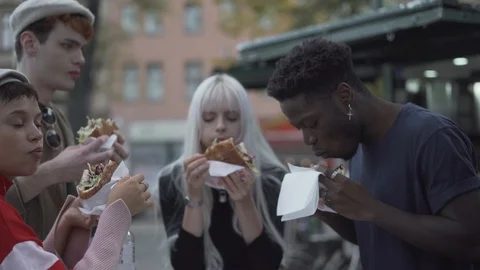 Handheld shot of hungry multiracial young friends eating sandwiches at outdoors Stock Footage 120435347