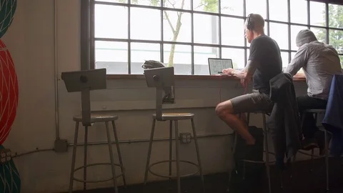 Handheld shot of male colleagues discussing over laptop computer by window at Stock Footage