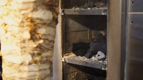 Handheld shot of man adding coals to shawarma skewer grill machine Stock Footage 121851790