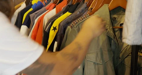 Handheld shot of man browsing and looking at jackets on rack Video stock 120068835