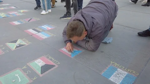A handheld shot of a man chalking flags of the world on the street in Stock Footage 119873342
