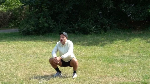 Handheld shot of man does squats in park Vídeo Stock 114849984