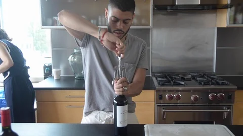 Handheld shot of a man opening bottle while a woman walking in the kitchen Vídeo Stock 115060184