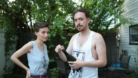 Handheld shot of man opens champagne bottle drinks it with his girlfriend Stock Footage 114862462
