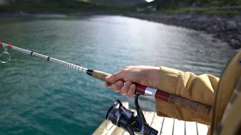 Handheld shot of a man using fishing rod for fishing and spinning the reel Stock Footage 114882191