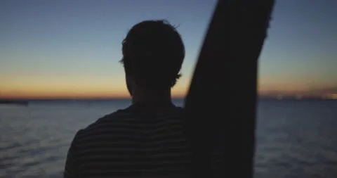 Handheld shot of man walking and holding guitar over his shoulder during sunset 스톡 동영상 147102399