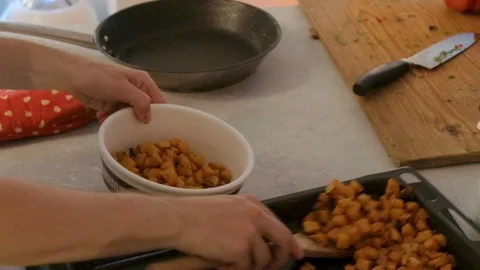 Handheld shot of mans hands spooning potato pieces from roasting pan into bowl 스톡 동영상 114867329