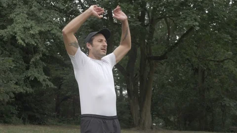 Handheld shot of mid adult man doing jumping jacks in park Stock Footage 114843053