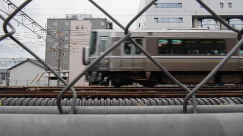 Handheld shot of passing train through chain fence with buildings in back, Japan Stock Footage 146138818