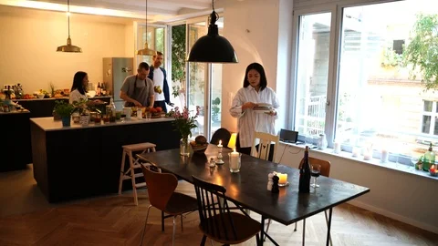 Handheld shot of people preparing dinner and setting dishes on table in kitchen Stock Footage 114883449