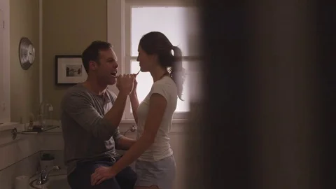 Handheld shot of playful couple talking while brushing teeth in bathroom Stock Footage