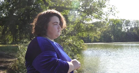 Handheld shot of plus size sad young woman standing by lake Stock Footage 120433362