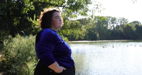 Handheld shot of plus size young woman smiling while standing near lakeside Stock Footage 120435737