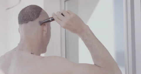 Handheld shot of professional surfer David Langer shaving his hair in mirror Stock Footage 160117074