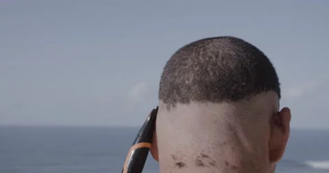 Handheld shot of professional surfer David Langer shaving his hair outside Stock Footage 160119039