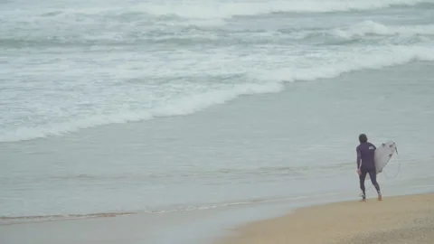 Handheld shot of professional surfer jogging towards seashore in wet suit Video stock 158651979
