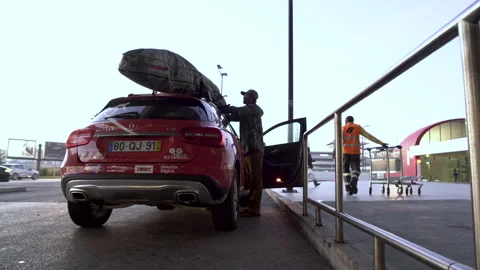 Handheld shot of professional surfer securing surfboard on top of car's vehicle Stock Footage 151086590