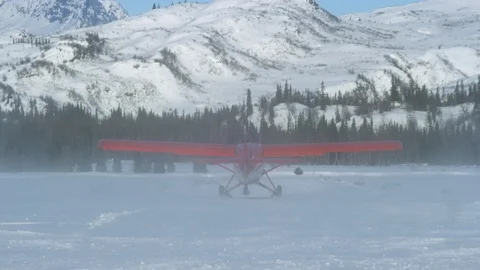Handheld shot of red airplane taking off on snowy land with mountains in back Stock Footage 129127834