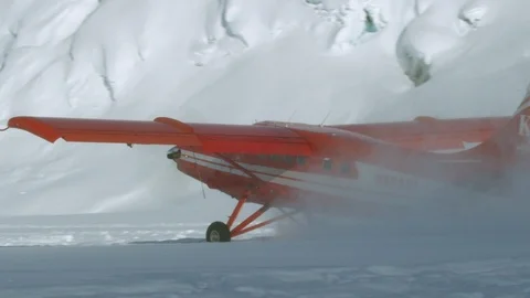 Handheld shot of red airplane taking off on snowy land near mountains, Alaska Видео 129128524