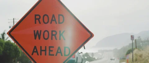 Handheld shot of road work ahead sign on road with cars passing in background Stock Footage 120288105