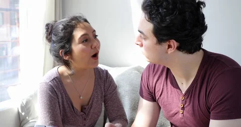 Handheld shot of romantic young couple talking and smiling while sitting on sofa Stock Footage 120428448