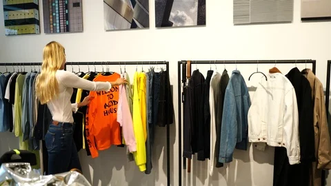 Handheld shot of sales clerk helping young woman about clothes in clothing shop Stock Footage 114883853