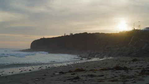 Handheld shot of sea waves reaching shore with people on cliff in background Stock Footage 120291041