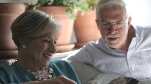Handheld shot senior couple reading magazine while sitting on sofa at home Stock Footage