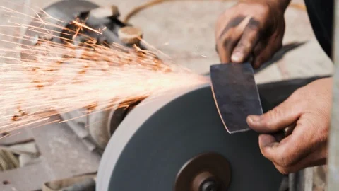 Handheld shot of skilled blacksmith sharpening knife blade as sparks fly out Stock Footage 147370601