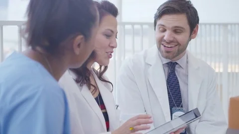 Handheld shot of smiling healthcare workers discussing over tablet computer in Stock Footage