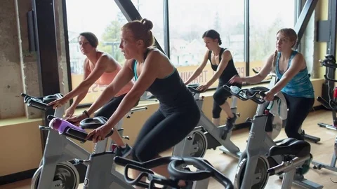 Handheld shot of smiling women cycling on exercise bikes at gym Stock Footage