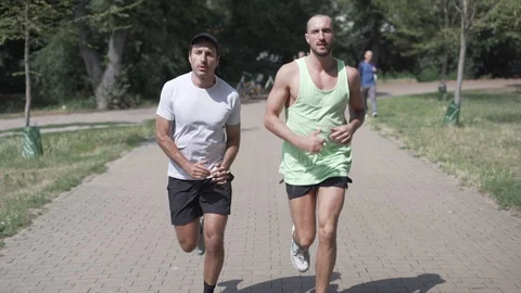 Handheld shot of two men jogging in park together Stock Footage 114878223