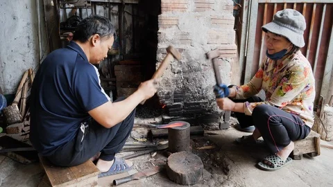 Handheld shot of two native vietnamese people working on flattening knife blade Stock Footage 147370358