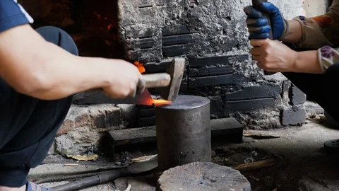 Handheld shot of two people pounding flat piece of metal to make knife blade Stock Footage 147372094