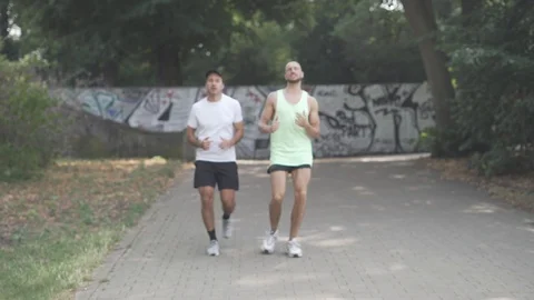 Handheld shot of two tired men jogging in park together Stock Footage 114878217